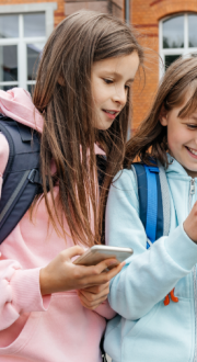 Two girls wearing backpacks and holding mobile phones