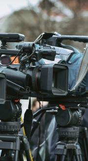 Several news cameras on tripods at an outdoor press conference.