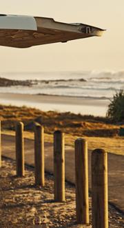 Man standing at the end of a van looking over a beach and talking on a mobile phone.