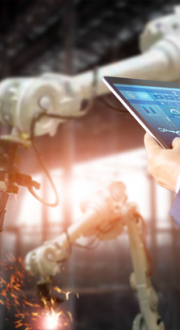 Man using a tablet in a factory to operate mechanical arms to do some welding work.