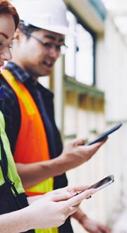 Woman and male tradies on a building site using mobile devices.