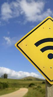 Wifi symbol on a yellow diamond shaped road sign in a rural setting next to a dirt road