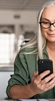 Woman sitting in front of laptop and looking at a mobile device in her hand.